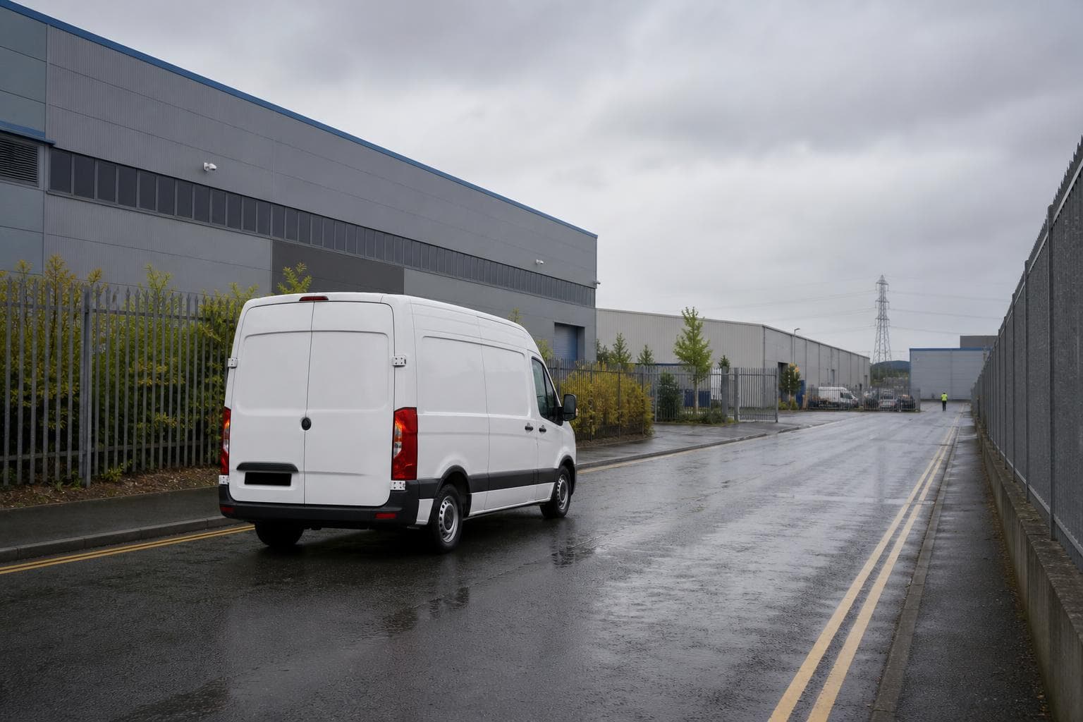 Unbranded courier van driving along a quiet Purfleet warehouse access road with wet UK road markings