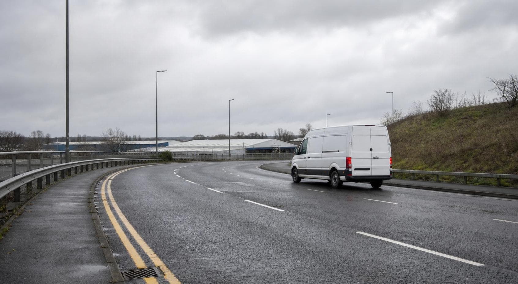 Unbranded courier van traveling on a broad South Ockendon estate road with wet asphalt and UK road markings